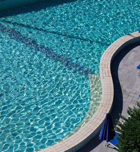 Pool with blue umbrellas and sunbeds, person relaxing.